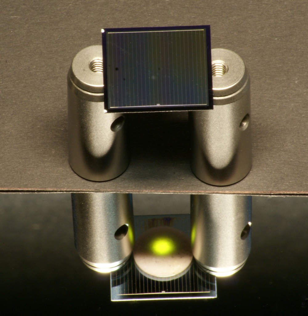 Eine zweiseitige Silicium-Solarzelle – hier aufgelegt auf Aluminium-Zylindern – wird von oben mit einem Infrarotlaser beleuchtet. 