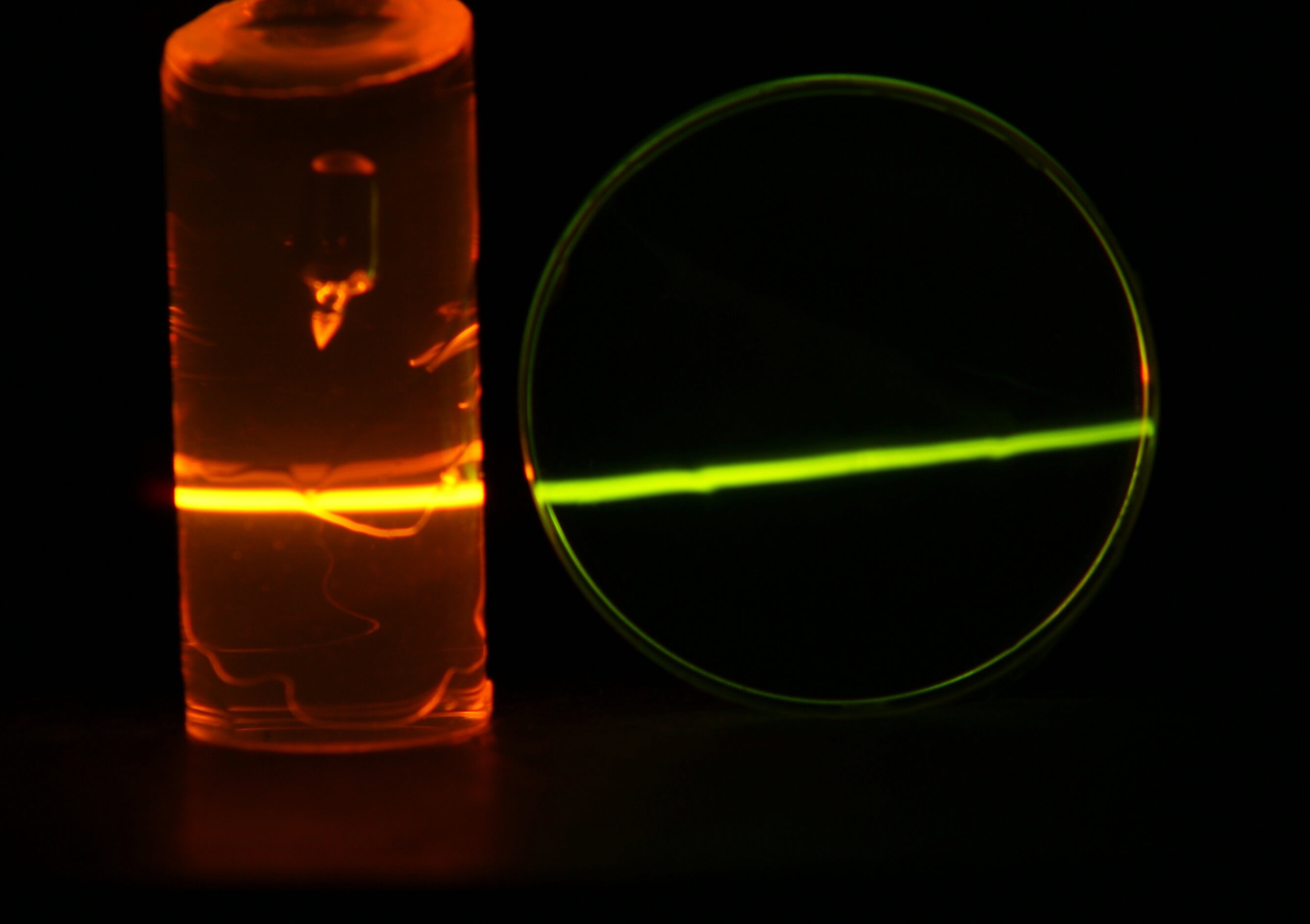 An invisible infrared laser beam, coming from the left, is incident on two PMMA upconverter samples. In the upconverter samples the laser ray is visible to the naked eye due to upconversion.